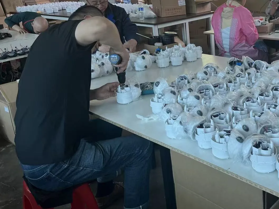 A worker driving screws into a camping shower pump housing, with rows of assembled housings on the bench at the Barong Yekhna plant in Jilin, China